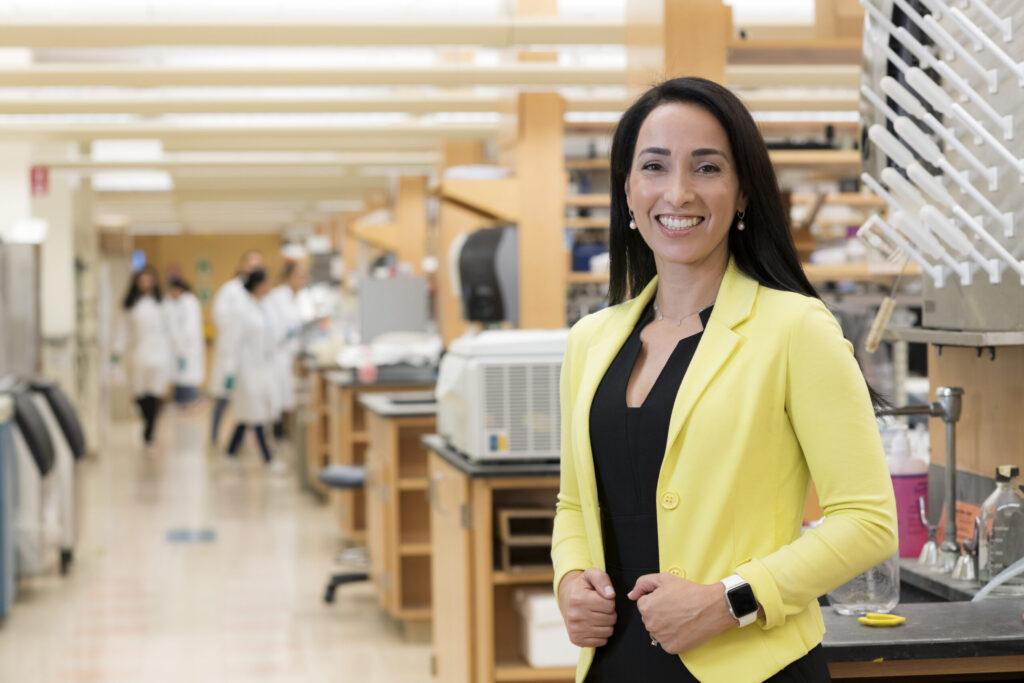 Natalie Artzi, PhD stands, in focus, in front of her blurred laboratory.